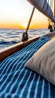 Sailboat deck at sunset with striped blue cushions and wooden trim against orange horizon and ocean waves, creating peaceful nautical atmosphere.