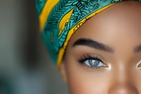 Close up portrait of young African woman with bright blue eyes wearing yellow and turquoise headwrap with palm leaf pattern, soft beauty makeup look.