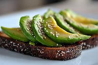 Fresh sliced avocado with sesame seeds on dark rye bread toast, healthy breakfast or snack option served on white plate, macro food photography.