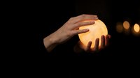 Hands gently holding glowing orb of warm light against dark background creating magical atmosphere for spiritual and energy healing concepts.