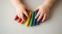 Child hands arranging colorful rainbow crayons in row on neutral background for creative art education and learning activities.