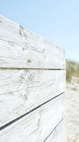 Weathered wooden beach fence with horizontal planks showing natural grain and knots, set against sandy dunes and clear sky. Suitable for coastal, rustic, and outdoor design projects.