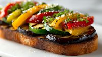 Grilled vegetable open sandwich with colorful bell peppers, zucchini and eggplant on toasted bread, garnished with herbs and cheese for healthy eating.