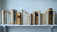 Row of vintage books in neutral beige and white colors arranged on white shelf against light wall, creating minimalist aesthetic for home decor and interior design.