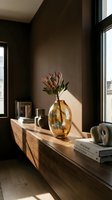 Modern minimalist interior with amber glass vase holding protea flowers on wooden console table against dark brown wall, sunlit styling for home decor and design inspiration.