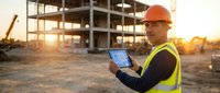 Construction engineer using tablet at building site during golden hour sunset for project management and digital planning workflows.