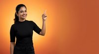 Young Indian woman in black shirt pointing upward with finger on orange gradient background for presentations and advertising campaigns.