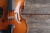 Classical violin with polished wooden body against rustic wooden background, showcasing fine craftsmanship and elegant curves of the instrument.