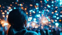 Young Asian woman watching fireworks display with bokeh lights in night sky, view from behind creating atmospheric festive mood in blue tones.