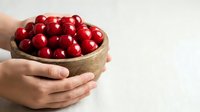 Close-up of hands holding rustic bowl filled with fresh red apples against white background, suitable for food, agriculture, harvest, and healthy eating content.