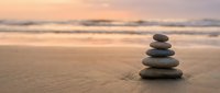Zen stone stack on sandy beach at sunset with soft ocean waves creating peaceful meditation and mindfulness atmosphere for wellness and spiritual balance.