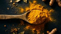 Golden turmeric powder in wooden spoon with fresh roots on dark slate surface. Aromatic cooking spice for healthy recipes and natural remedies.