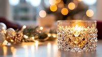 Glowing crystal candle holder with warm light and festive bokeh background, golden Christmas decorations and string lights creating cozy holiday atmosphere.