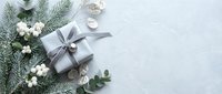Elegant Christmas gift box with silver ribbon surrounded by pine branches, white flowers and eucalyptus on marble background for holiday celebrations.