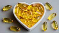 Heart-shaped bowl filled with golden omega-3 fish oil capsules surrounded by scattered supplements on white background for health and wellness.
