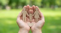 Hands holding wooden family figures in protective gesture outdoors symbolizing care, support and unity in natural green environment for insurance concepts.