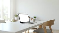 Modern minimalist home office workspace with open laptop computer on white desk and wooden chair in bright natural light interior.