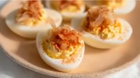 Creamy deviled eggs garnished with paprika and tuna flakes served on ceramic plate, close up view of classic appetizer for party or holiday celebration.