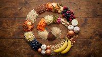 Colorful circle of fresh fruits, vegetables, grains, and nuts arranged on a wooden table, showcasing a balanced diet and healthy nutrition concept.