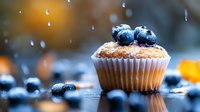 Fresh baked vanilla muffin topped with ripe blueberries and powdered sugar on dark reflective surface with water drops and warm bokeh background.