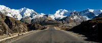 Straight asphalt road stretching through high mountain valley with snow-capped peaks under clear blue sky. Suitable for travel, adventure, and landscape design projects.