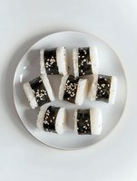 Fresh sushi rolls with nori seaweed and white rice garnished with sesame seeds arranged on round white ceramic plate against light background.