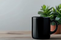 Black ceramic coffee mug on wooden table with green plant in background, minimalist composition for cafe, restaurant or home decor marketing.
