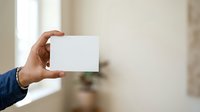 Cropped hand of male professional holding blank white business card against neutral beige background for corporate branding and marketing presentations.