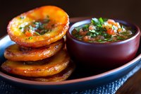 Crispy fried corn tortillas stacked on ceramic plate with fresh salsa roja in traditional clay bowl, garnished with cilantro and chopped onions, Mexican cuisine.