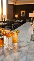 Elegant cocktails on marble bar counter in upscale restaurant with warm ambient lighting and sophisticated interior design for hospitality industry.