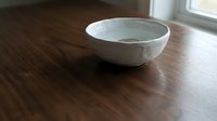 White ceramic bowl sitting on dark wooden table surface near window with natural light casting soft shadows.