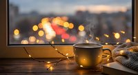 Cozy winter evening scene with steaming coffee mug and warm fairy lights by window overlooking blurred city lights at sunset for relaxation and comfort themes.