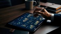 Business professional analyzing financial data on tablet with charts and graphs in modern office workspace for investment planning and market research.
