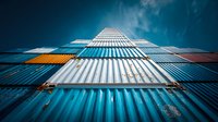 Modern shipping container skyscraper with colorful metal panels against dramatic blue sky for urban architecture and logistics industry concepts.