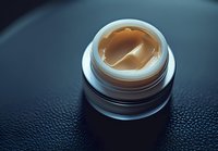 Luxurious cream jar with golden moisturizer on dark textured background, close-up view showing premium skincare product consistency and texture.