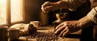 Elderly man grinding fresh coffee beans with traditional hand grinder in warm sunlit kitchen, artisanal coffee preparation process for morning brew ritual.