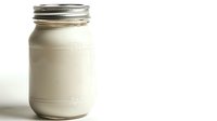 Fresh dairy milk in classic glass mason jar with metal lid on white background, minimalist food photography style for packaging and beverage concepts.