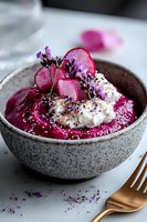 Vibrant beetroot smoothie bowl topped with whipped cream, pickled radish slices, lavender flowers, and purple garnish in gray ceramic bowl. Food styling.
