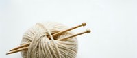 Ball of beige wool yarn with wooden knitting needles on white background, isolated crafting supplies for handmade projects and creative hobbies.