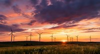 Wind turbines generating renewable energy at sunset with dramatic colorful sky over golden wheat field creating sustainable power landscape.