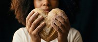 Young African American woman holding fresh artisan bread loaf with both hands against dark background for bakery and food photography concepts.
