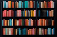 Colorful vintage hardcover books arranged on dark wooden library shelves creating vibrant pattern of spines in coral, teal, yellow and blue tones against black background.