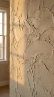 Textured plaster wall with peeling paint and natural light casting shadows, suitable for backgrounds, interior design projects, and architectural photography.