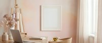 Minimalist home office workspace with blank white frame mockup on pink wall, wooden desk, laptop, dried flowers in vase, and natural lighting for branding.