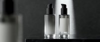 Elegant glass cosmetic bottles with pump dispensers on dark surface in dramatic lighting for luxury skincare and beauty product packaging design.
