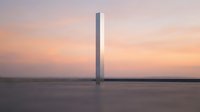 Minimalist architectural structure standing alone in vast empty landscape during golden hour sunset with soft pastel sky and calm water reflection.