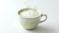 Matcha latte with creamy foam in ceramic cup on white background, suitable for beverage, cafe, and wellness marketing.