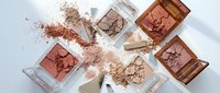Cosmetic powder makeup palette collection with bronze and nude shades scattered on white background for beauty and fashion applications.