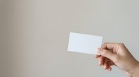 Woman's hand holding blank white business card against neutral beige background for branding, corporate identity, and marketing mockup purposes.