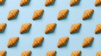 Golden croissants arranged in repeating pattern on light blue background, ideal for bakery, cafe, food business branding and culinary design projects.